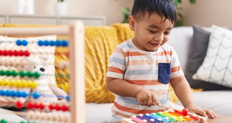 Adorable hispanic toddler playing xylophone standing at home
